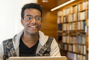 Simon sitter på ett bibliotek och studerar. Foto.