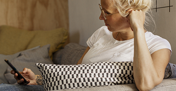 Kvinna i vit t-shirt sitter i en soffa och tittar i sin mobil.