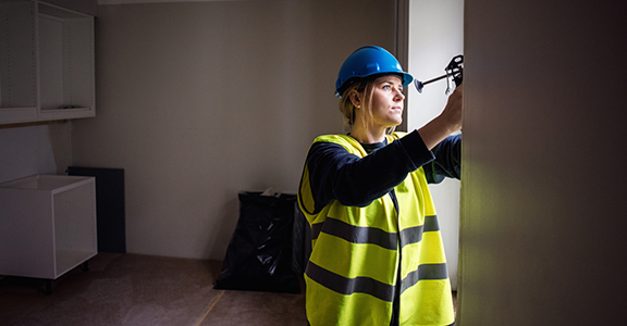 Kvinnlig byggjobbare i hjälm och gul reflexväst arbetar inomhus